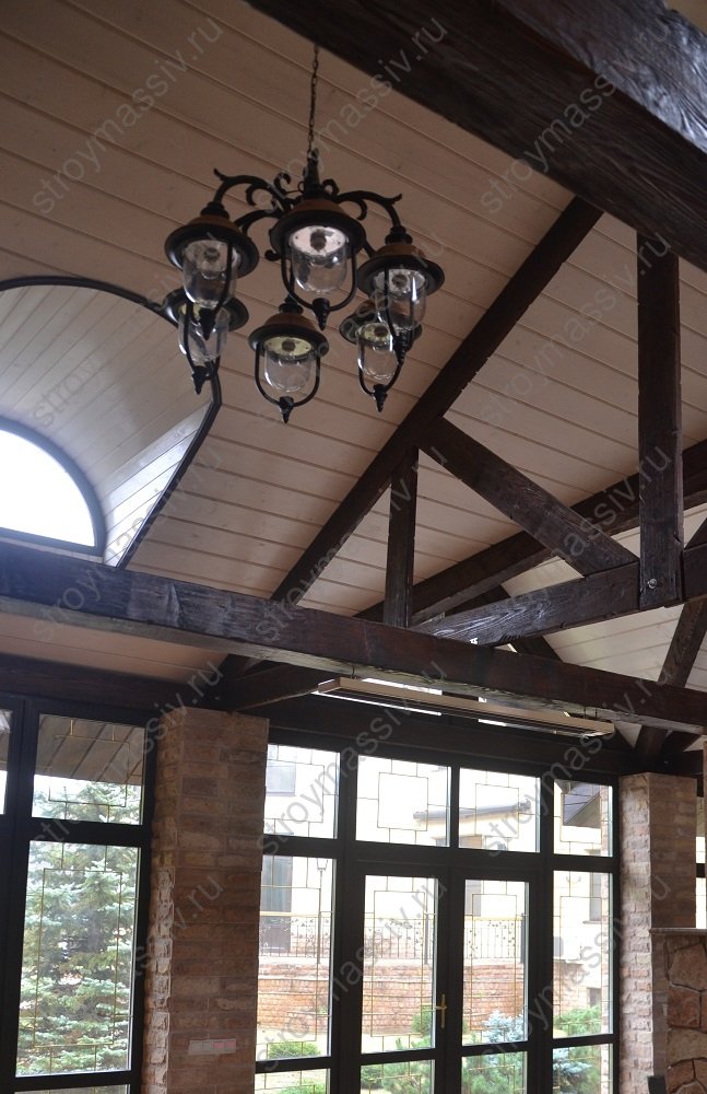 Скошенный потолок с декоративными балками в теплой беседке-павильоне